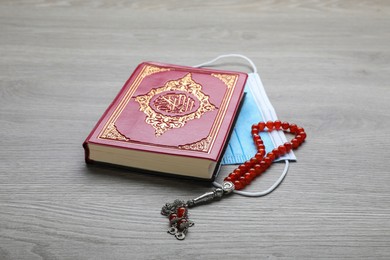 Muslim prayer beads, Quran and medical mask on wooden table