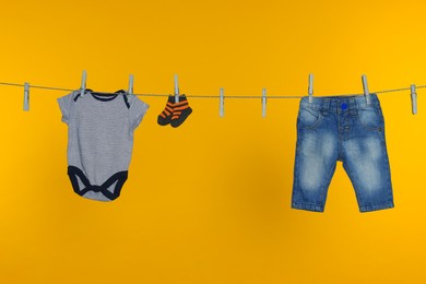 Different baby clothes drying on laundry line against orange background
