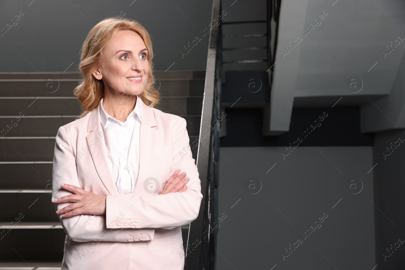 Photo of Happy lady boss near staircase indoors, space for text. Successful businesswoman