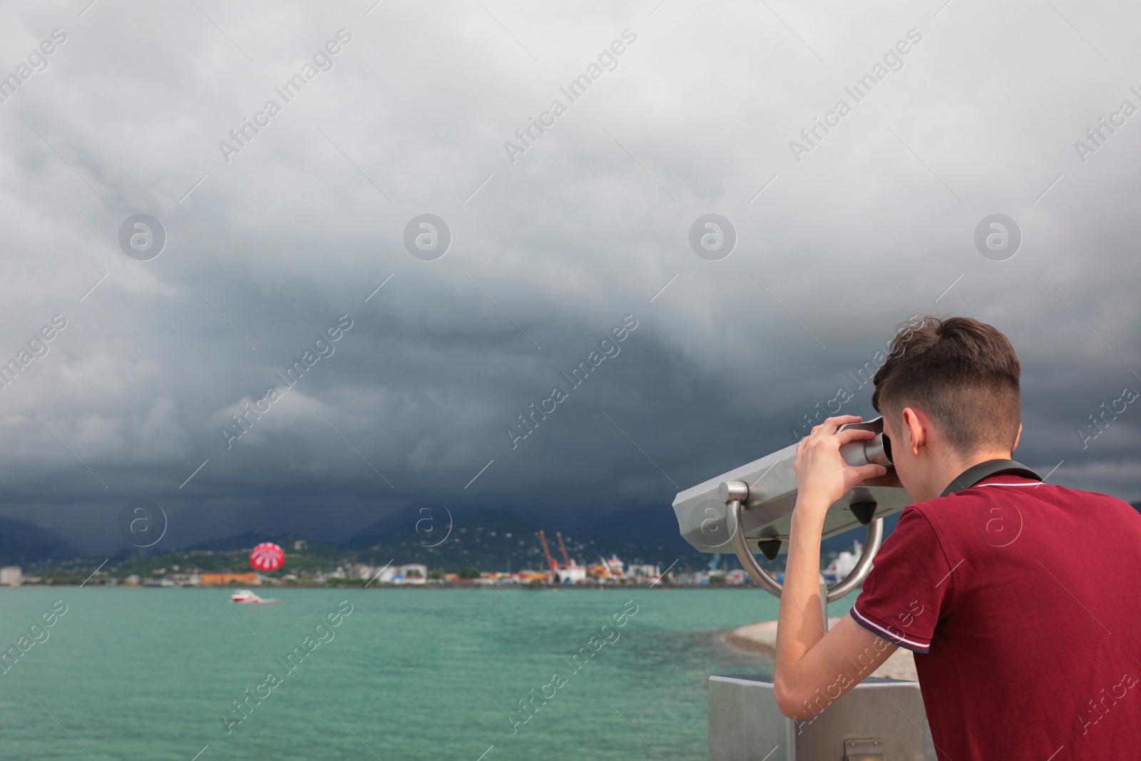 Photo of Teenage boy looking through mounted binoculars at mountains. Space for text