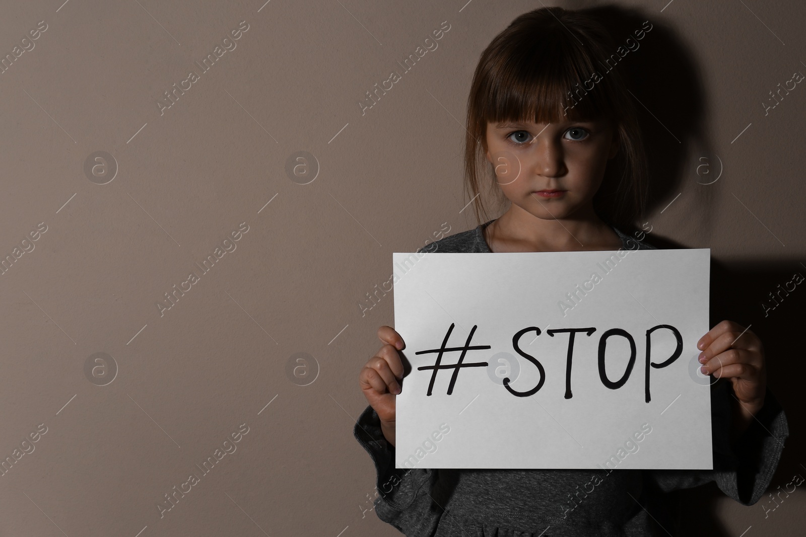 Photo of Abused little girl with hashtag STOP near beige wall, space for text. Domestic violence concept