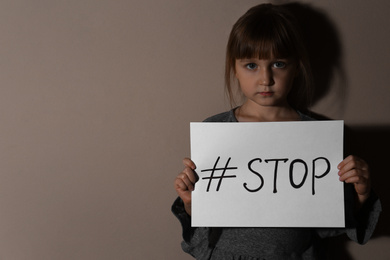 Photo of Abused little girl with hashtag STOP near beige wall, space for text. Domestic violence concept