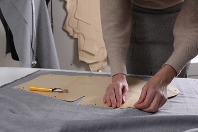 Photo of Tailor pinning sewing pattern to fabric at table in atelier, closeup