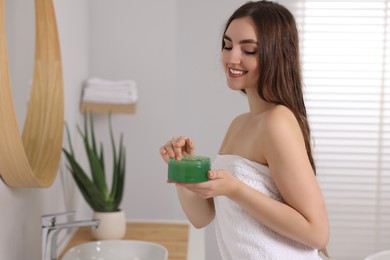 Photo of Young woman holding jar of aloe hair mask near mirror in bathroom