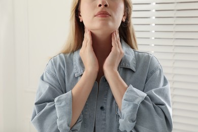 Photo of Young woman doing thyroid self examination near window indoors, closeup