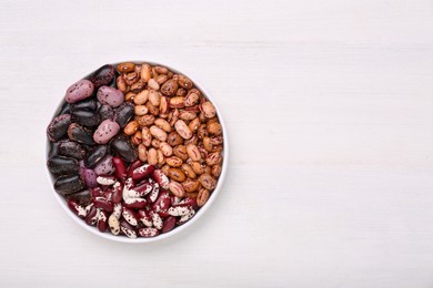 Bowl with different types of beans on white wooden table, top view. Space for text