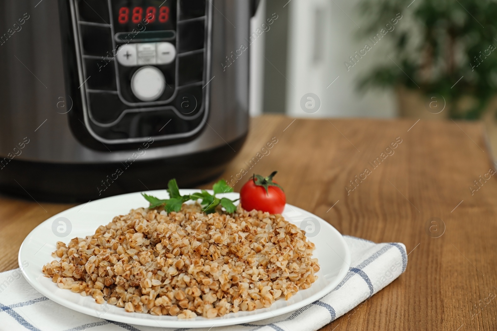 Photo of Plate with delicious buckwheat and multi cooker on wooden table. Space for text