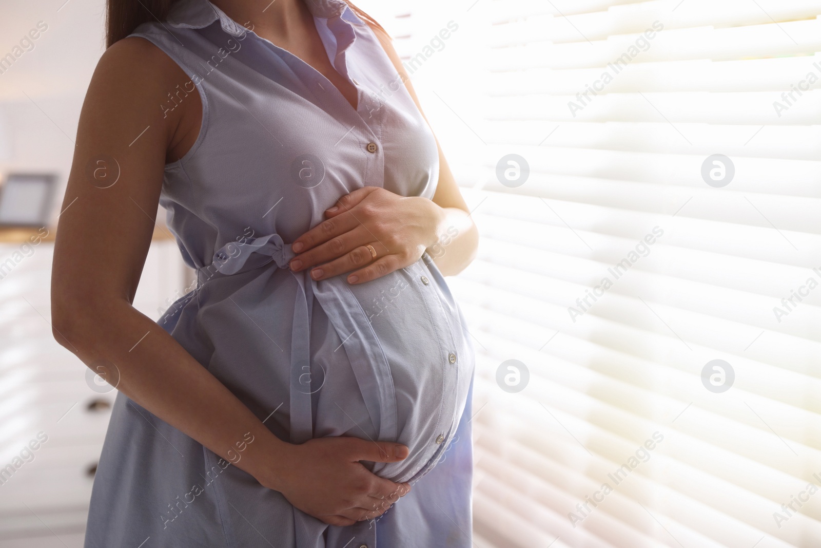 Photo of Young pregnant woman near window indoors, closeup. Space for text