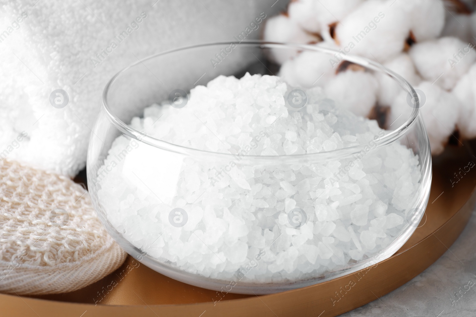 Photo of White sea salt for spa scrubbing procedure in glass bowl on grey table