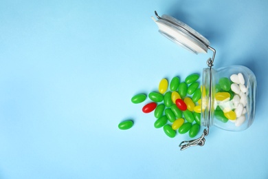 Photo of Overturned jar with jelly beans on color background, top view. Space for text