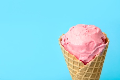 Photo of Delicious pink ice cream in waffle cone on light blue background, closeup. Space for text