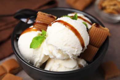 Photo of Bowl of tasty ice cream with caramel sauce, candies and mint on table, closeup