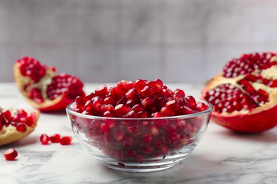 Ripe juicy pomegranate grains in bowl on white marble table