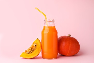 Tasty pumpkin juice in glass bottle, whole and cut pumpkins on pink background