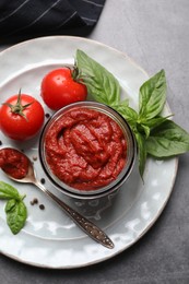 Photo of Jar of tasty tomato paste and ingredients on gray table, top view