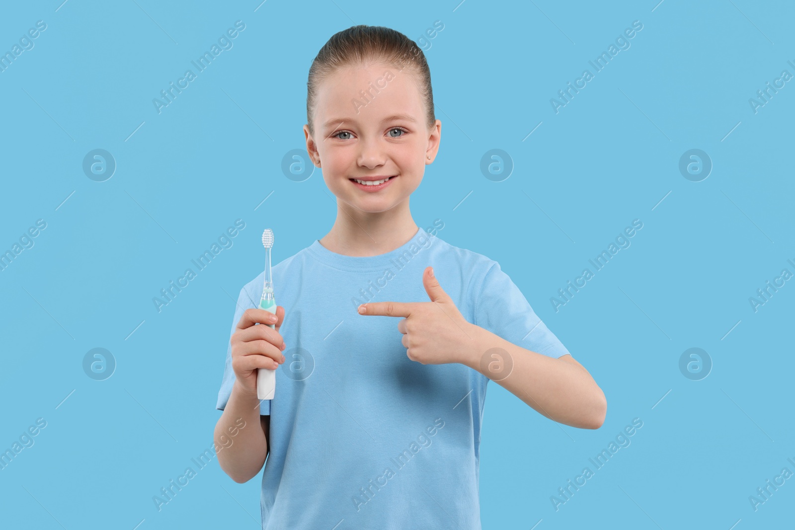 Photo of Happy girl holding electric toothbrush on light blue background