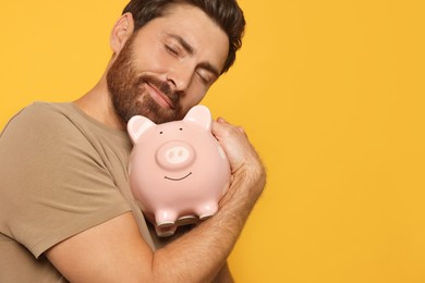 Photo of Happy man with ceramic piggy bank on orange background, space for text
