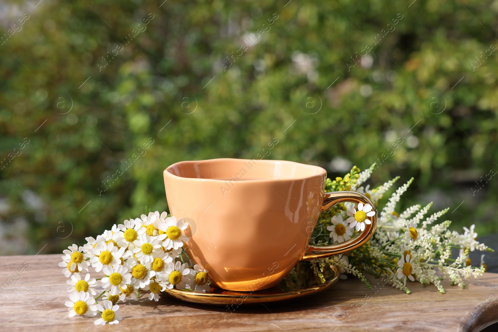 Photo of Cup of delicious chamomile tea and fresh flowers outdoors on sunny day