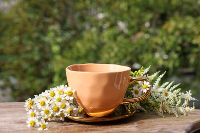 Cup of delicious chamomile tea and fresh flowers outdoors on sunny day