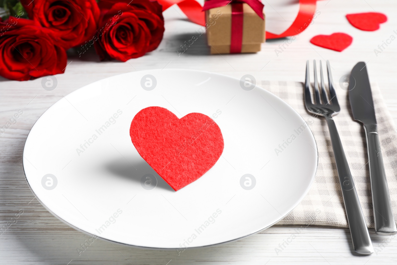 Photo of Beautiful place setting with dishware, gift and bouquet for romantic dinner on white wooden table