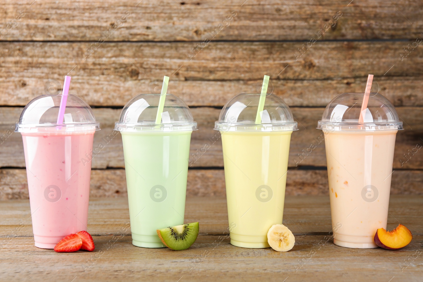 Photo of Plastic cups with different tasty smoothies and fresh fruits on wooden table