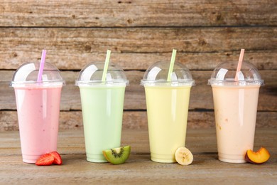 Photo of Plastic cups with different tasty smoothies and fresh fruits on wooden table