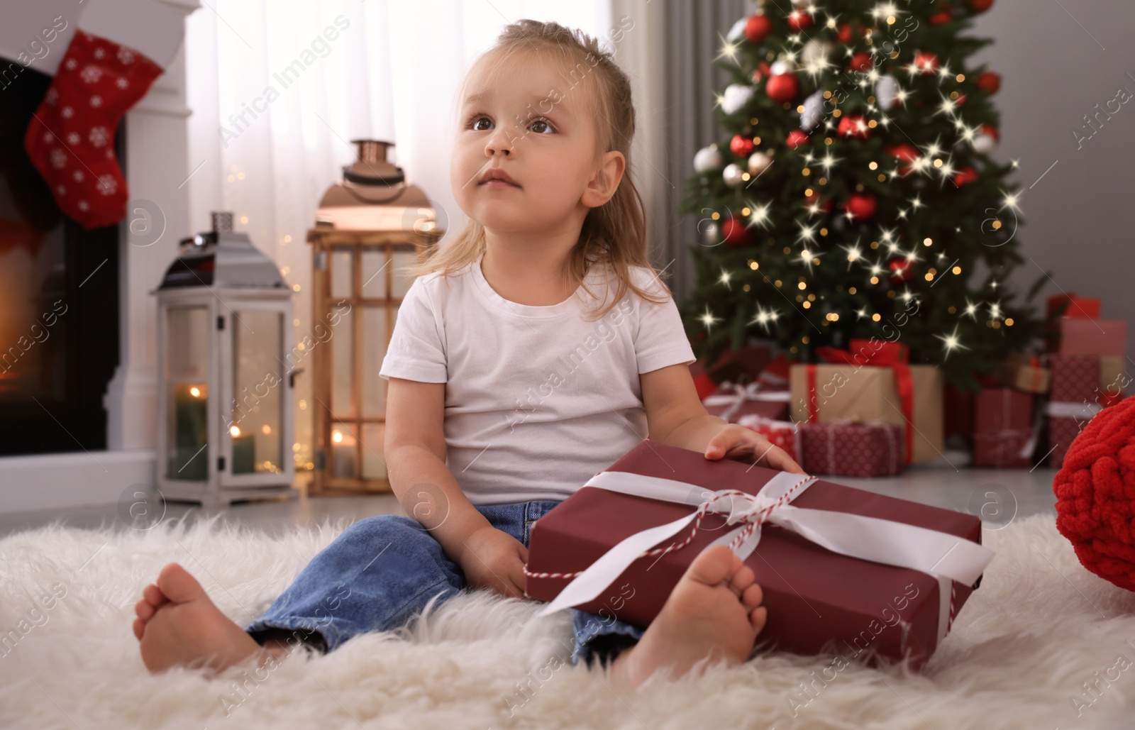 Photo of Cute little girl with Christmas gift in festively decorated room