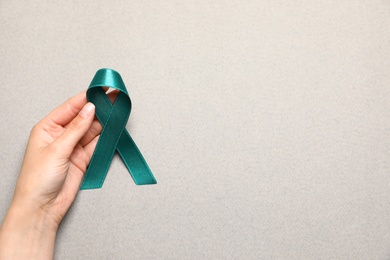 Photo of Woman holding teal awareness ribbon on grey paper, top view with space for text. Symbol of social and medical issues