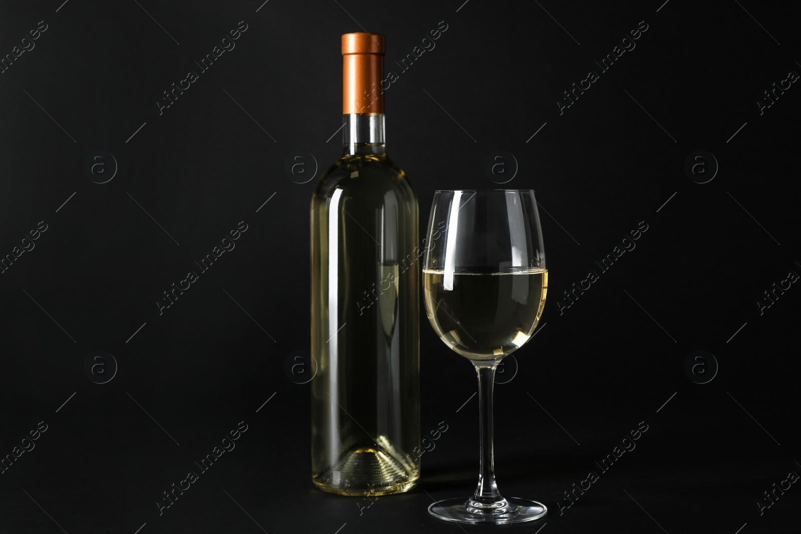 Photo of Bottle and glass of expensive white wine on dark background