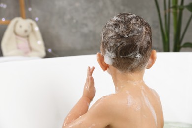 Photo of Cute little boy washing hair with shampoo in bathroom, back view