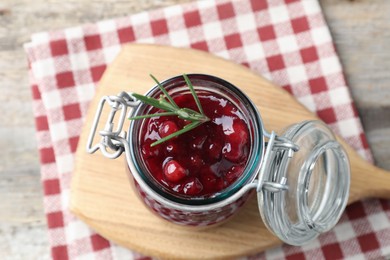 Photo of Fresh cranberry sauce in glass jar and rosemary on table, top view