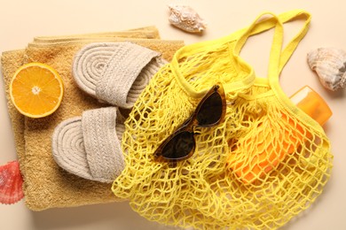 String bag, different beach accessories and orange on beige background, top view