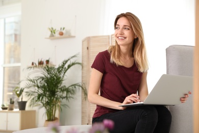 Photo of Young woman using laptop at home, space for text. Trendy room interior with plants