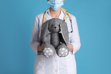 Photo of Pediatrician with toy bunny and stethoscope on light blue background, closeup
