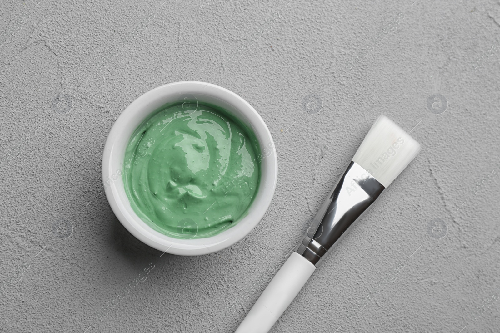 Photo of Spirulina facial mask and brush on light grey table, flat lay