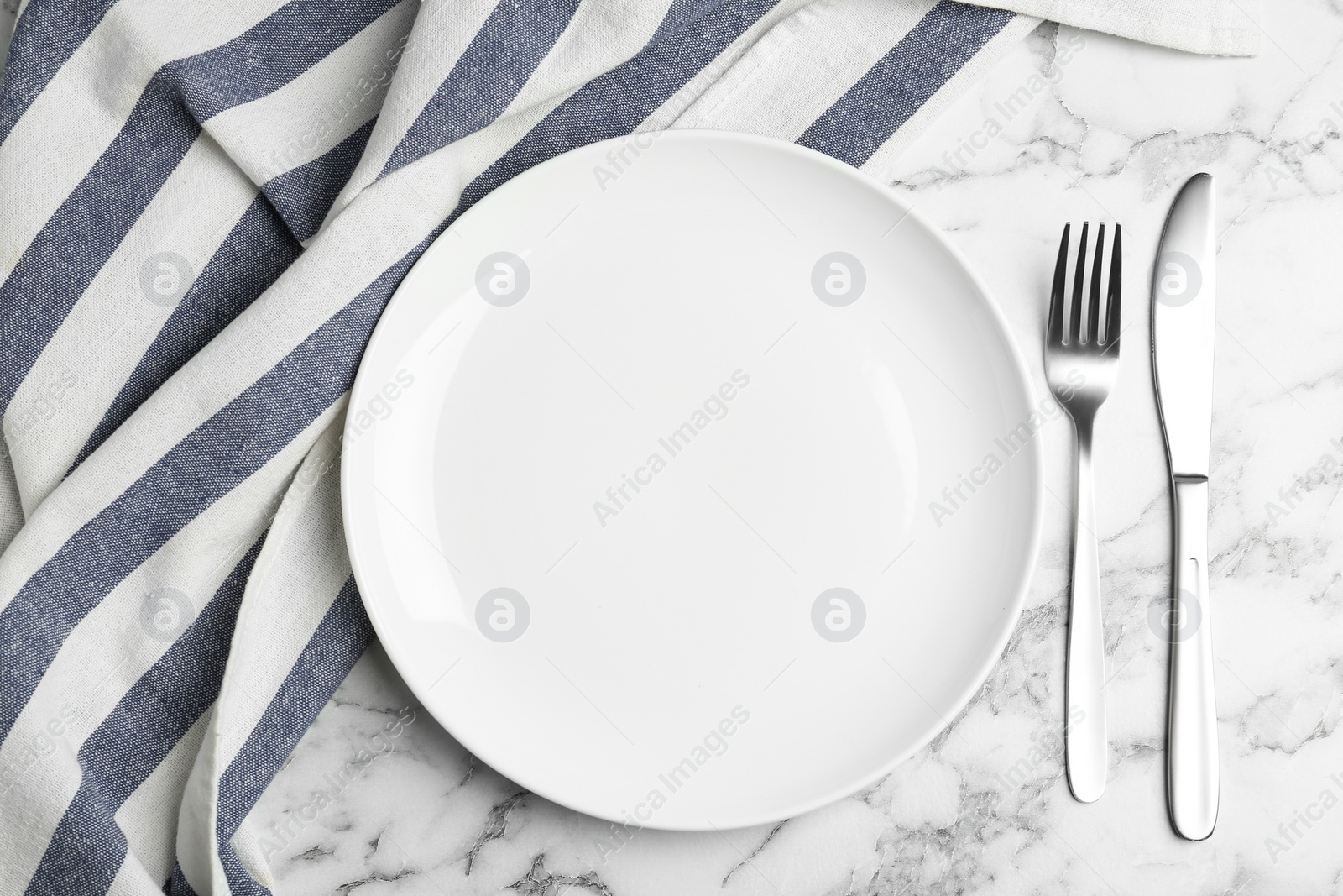 Photo of Empty plate with cutlery and fabric on white marble table, flat lay