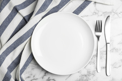 Photo of Empty plate with cutlery and fabric on white marble table, flat lay