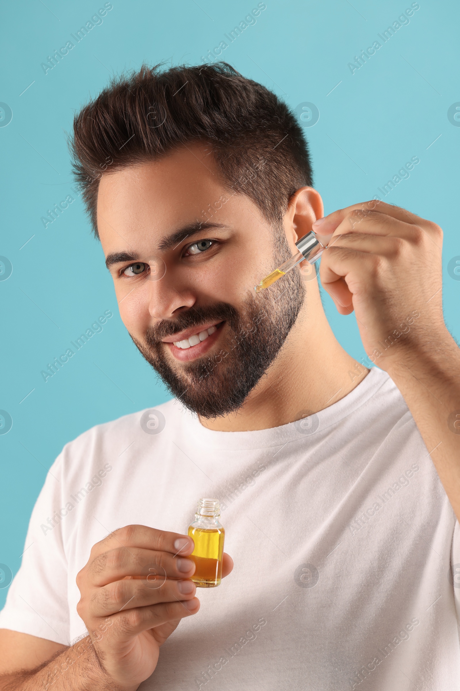 Photo of Handsome man applying cosmetic serum onto face on light blue background
