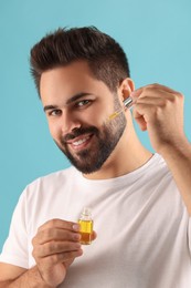 Handsome man applying cosmetic serum onto face on light blue background