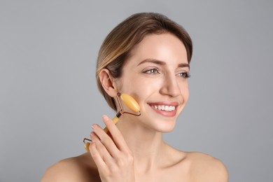Young woman using natural jade face roller on light grey background
