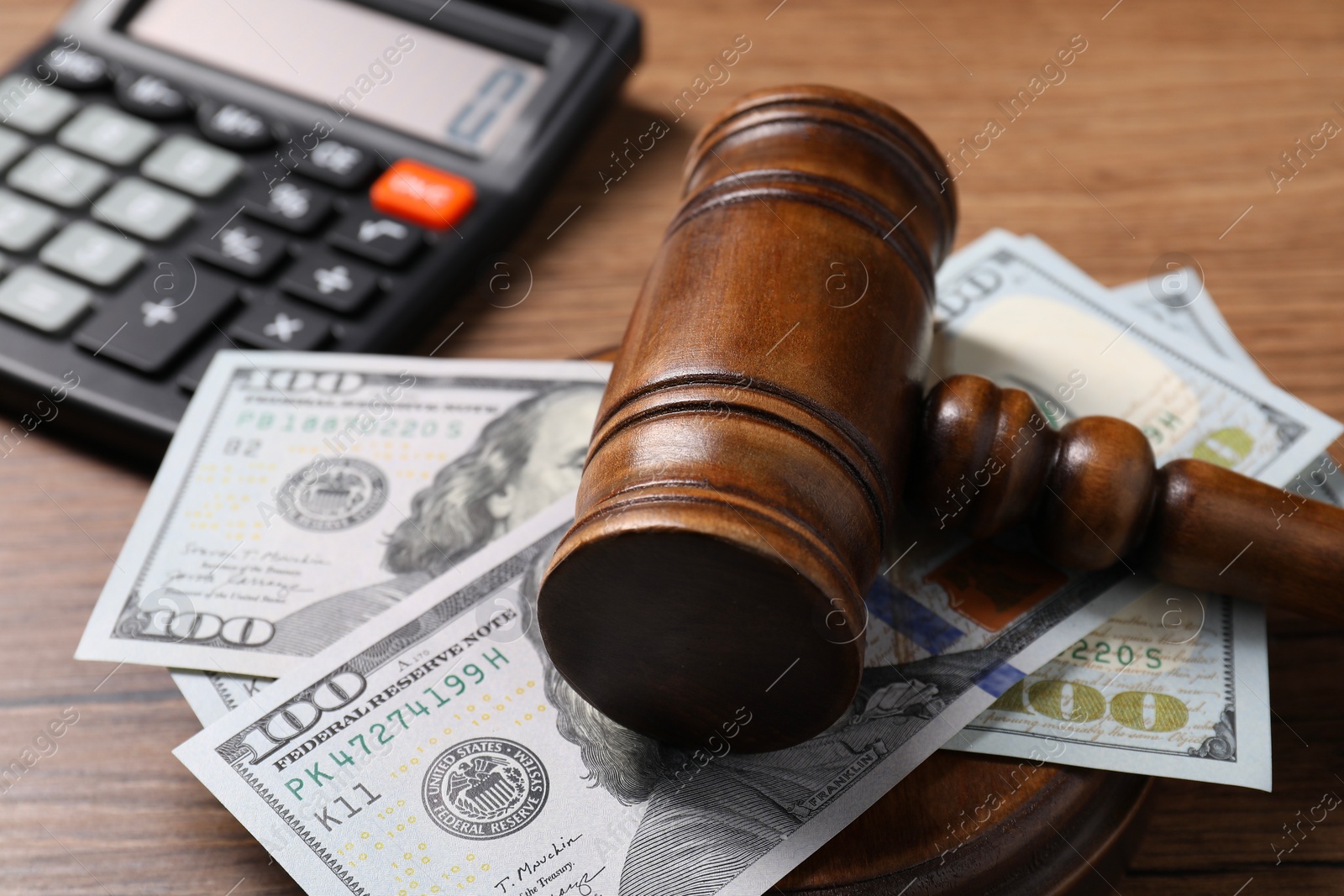 Photo of Tax law. Gavel, dollar banknotes and calculator on wooden table, closeup