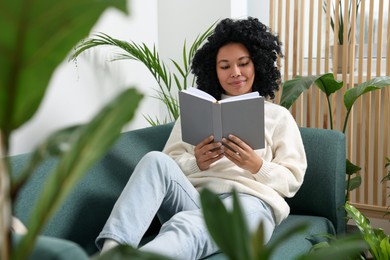 Relaxing atmosphere. Woman reading book on sofa surrounded by beautiful houseplants in room