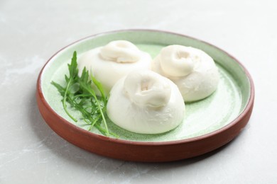 Photo of Delicious burrata cheese with arugula on light table, closeup