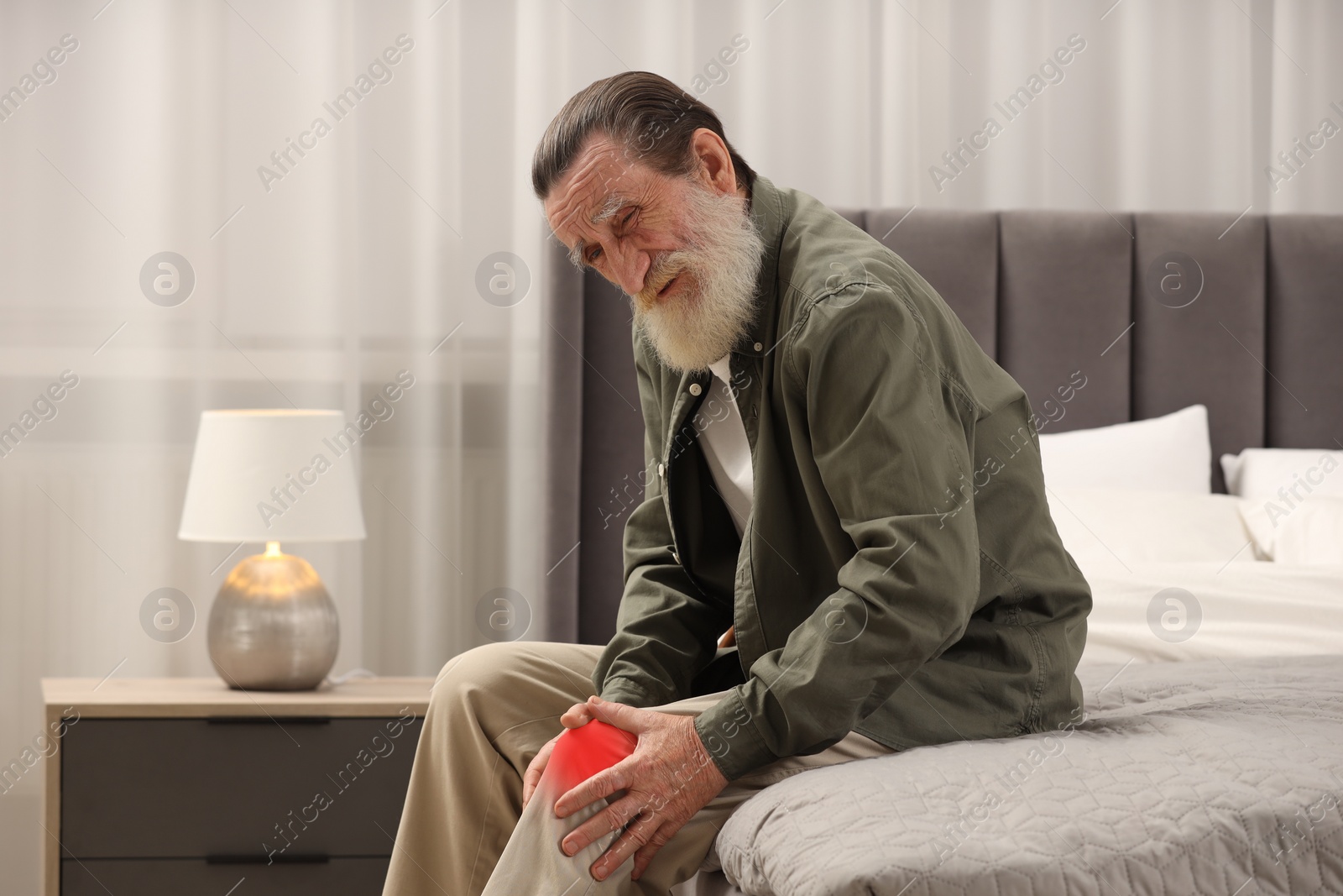 Image of Senior man suffering from pain in knee on bed at home