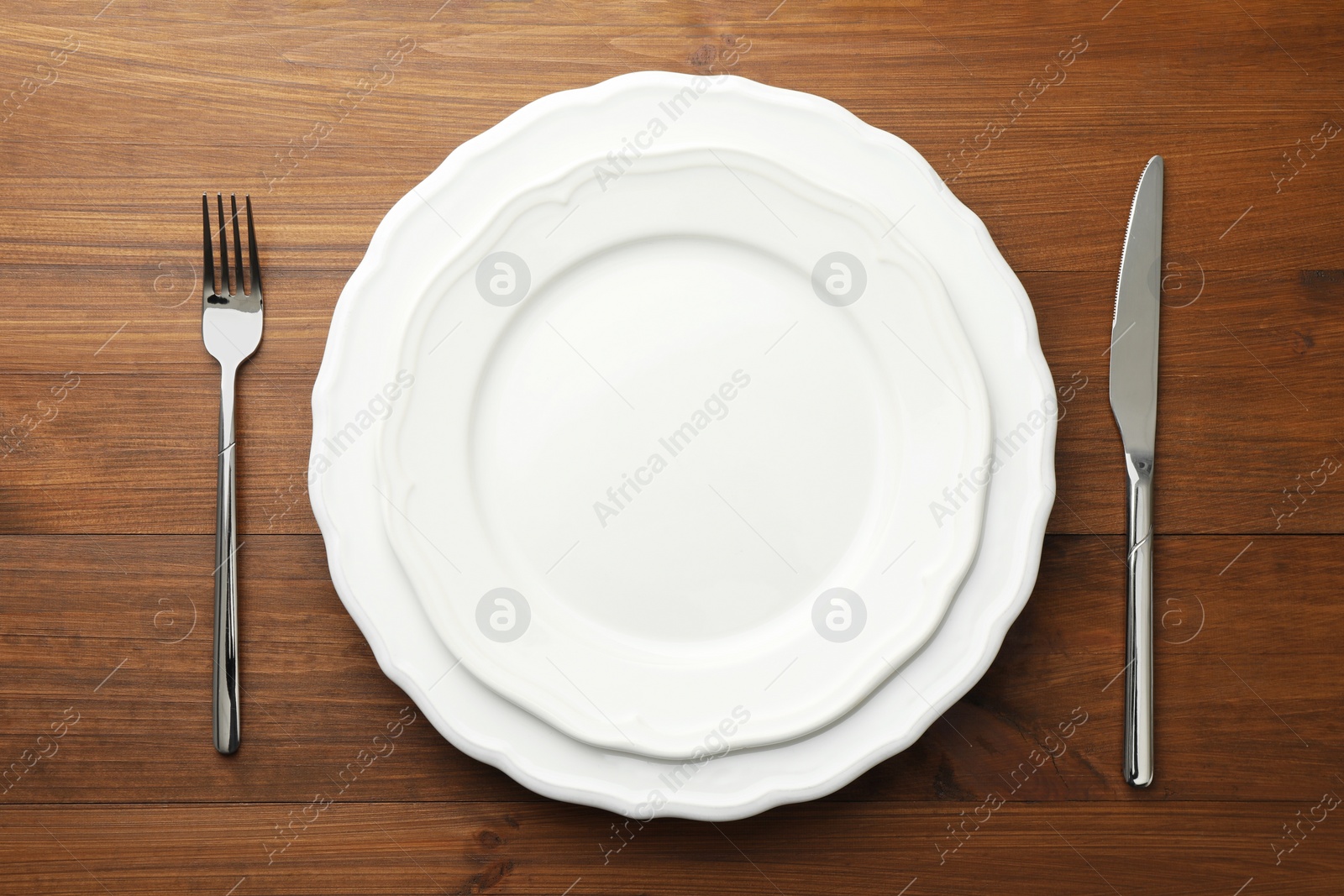 Photo of Clean plates, fork and knife on wooden table, top view