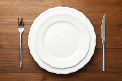 Clean plates, fork and knife on wooden table, top view