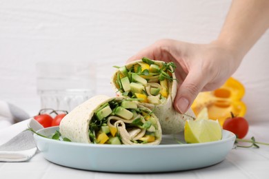 Photo of Woman holding delicious sandwich wrap with fresh vegetables at white tiled table, closeup