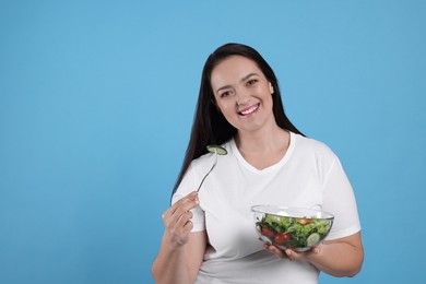 Photo of Beautiful overweight woman eating salad on light blue background, space for text. Healthy diet