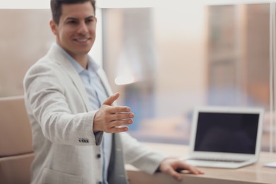 Photo of Businessman offering handshake in office, focus on hand. Space for text