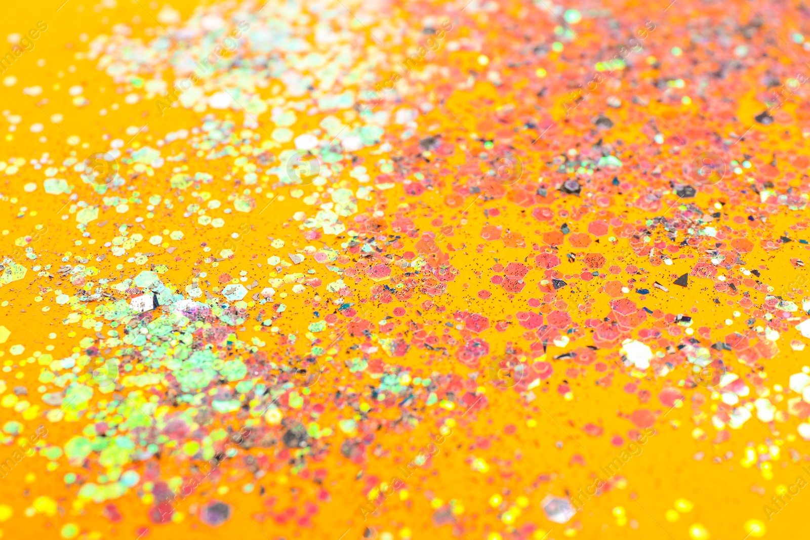 Photo of Shiny bright glitter on yellow background, closeup